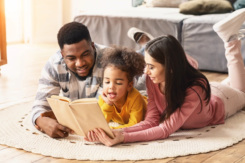 familia deitada no chao lendo livro com a filha