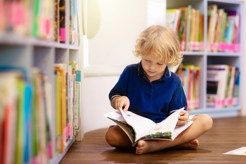 menino lendo um livro no chao da biblioteca