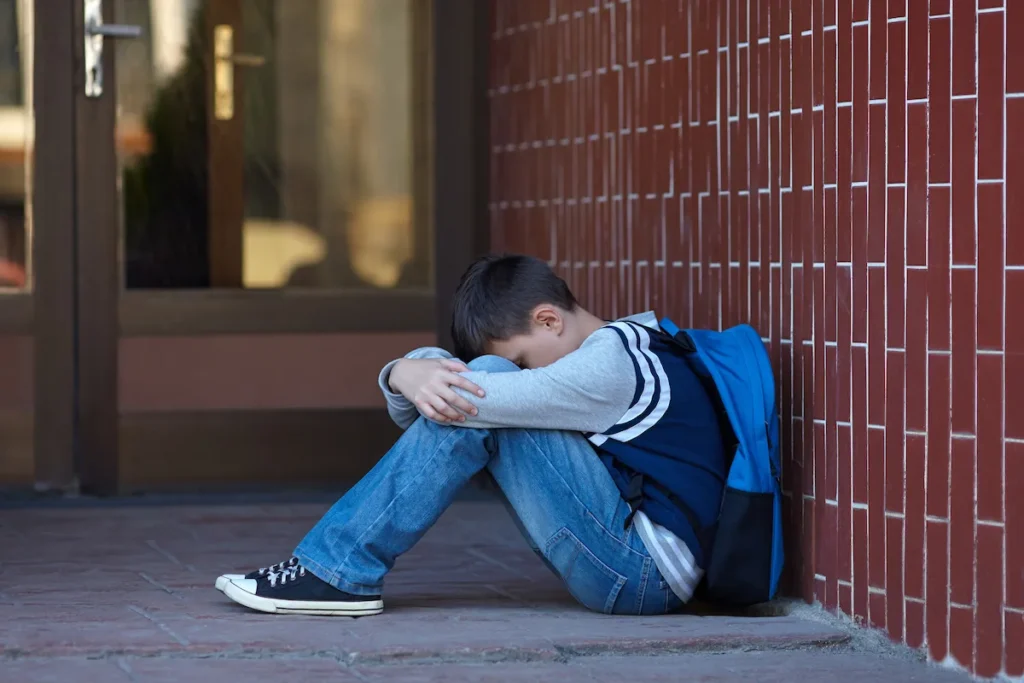 aluno sentado encostado na parede com a cabeça entre as pernas chorando