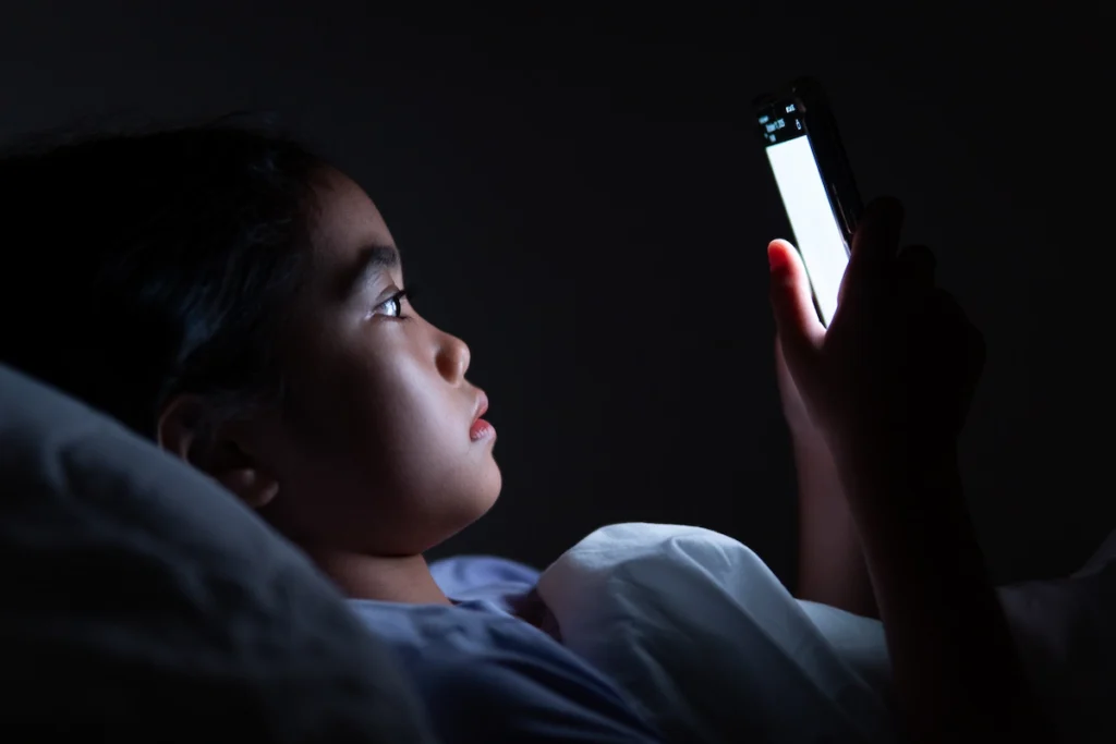 menina deitada na cama usando o celular