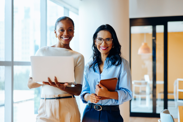 Duas mulheres, sorrindo, em, um, escritório, segurando, laptop, e, notebook